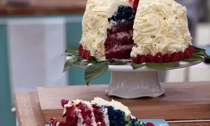 En skivad red velvet cake med vit frosting, hallon och blått inuti. En bit ligger på en blå tallrik.
