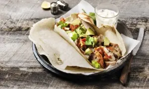 Tortilla z kurczakiem, awokado i sosem na drewnianym stole.
