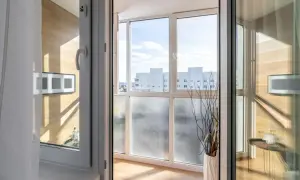 Zabudowany balkon z widokiem na budynki, ozdobiony wazonem z gałązkami.