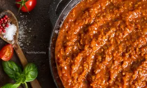 Herzhafte Bolognese-Sauce in einer Pfanne, mit frischen Tomaten, Basilikum, Salz und Pfefferkörnern als Zutaten für Bolognese.
