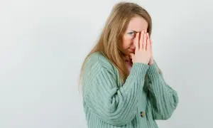 Een vrouw met blond haar, die haar gezicht bedekt met haar handen, lijkt overprikkeld, wat kan duiden op hsp en trauma.