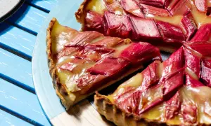 Une tranche de tarte à la rhubarbe, garnie de fruits rouges et d'une crème dorée, repose sur une assiette bleue.