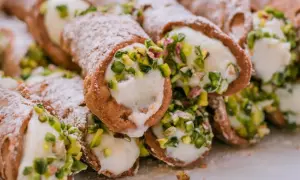 Stos delikatnych, włoskich rurek z kremem i pistacjami, posypanych cukrem pudrem.