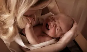 Matka tuli płaczące dziecko, szukając sposobu, jak odczynić urok na dziecku. Delikatne dłonie i włosy otulają maluszka.