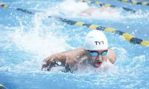 A swimmer in a white cap and goggles powers through the water, demonstrating technique for how to swim faster.