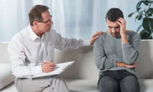 Psycholog dla dorosłych wspiera mężczyznę w trudnych chwilach. Terapeuta kładzie dłoń na ramieniu pacjenta, okazując zrozumienie i troskę.