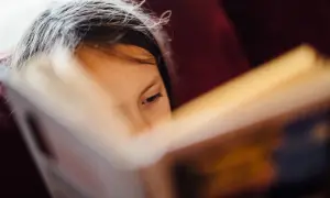 Niña concentrada en la lectoescritura, página de libro abierto.