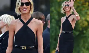 Elegancka kobieta w czarnej sukience i okularach przeciwsłonecznych, z subtelnymi złotymi akcentami, jak bransoleta i klamra paska.