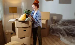 Donna con pianta in mano, circondata da scatoloni, in una casa in fase di trasloco. Potrebbe essere interessata alle agevolazioni prima casa senza residenza.