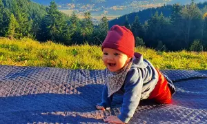 Uśmiechnięte dziecko na kocyku w górach. Jakby czytało psalm 131 tekst, pełne spokoju i radości.