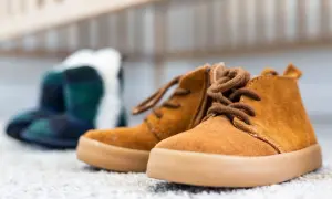Brązowe, sznurowane buty dziecięce na pierwszym planie, w tle niebiesko-zielone botki w kratę.