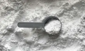 Miarka z białym proszkiem, prawdopodobnie tetrasodium glutamate diacetate, na tle sypkiego materiału.