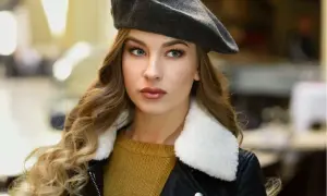 Elegancka kobieta w grafitowym beretu, z burzą blond włosów i w czarnej ramonesce. Pokazuje, jak nosić beret damski.