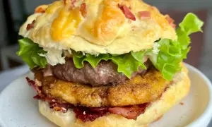 Domowy burger z serem, bekonem, kotletem i sałatą na talerzu.