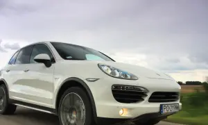 Biały Porsche Cayenne Turbo pędzi po drodze, chmury na niebie sugerują zmienną pogodę.