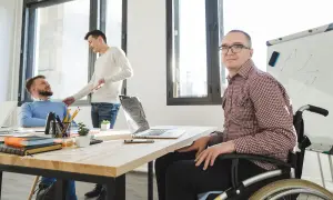 Ufficio inclusivo: un uomo in carrozzina, parte delle categorie protette art. 1, lavora con colleghi.