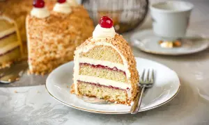 Ein Stück Frankfurter Kranz mit Buttercreme, Marmelade und gehackten Nüssen, garniert mit einer Kirsche.