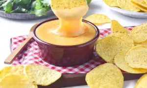 Un totopo se sumerge en una cremosa salsa cheddar, rodeado de más totopos y cilantro fresco.