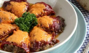 Pimientos rellenos de carne cubiertos con una cremosa salsa naranja, adornados con perejil fresco.