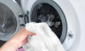Eine Hand hält ein weißes Hemd, bereit, es in die Waschmaschine zu legen. Die Tür der Waschmaschine ist geöffnet und gibt den Blick auf weitere Wäsche frei.