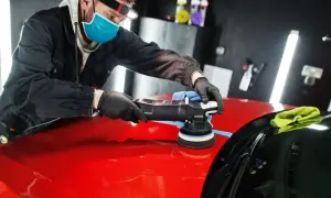 Mężczyzna w masce i rękawiczkach poleruje czerwony lakier samochodu polerką. Dobra jaka pasta polerska zapewni idealny połysk.