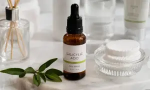 Serum z kwasem salicylowym 2% do twarzy, obok waciki i zielona gałązka.
