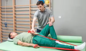Fizjoterapeuta pomaga pacjentowi w ćwiczeniach z gumą oporową na łóżku rehabilitacyjnym.