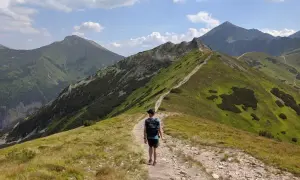 Wędrowiec na szlaku prowadzącym na **ornak szczyt**. Zielone zbocza górskie, kamienista ścieżka i błękitne niebo z chmurami.