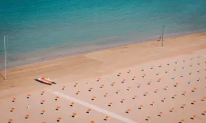 Pusta plaża w Rimini z rzędem pomarańczowych parasoli i małą łodzią motorową.