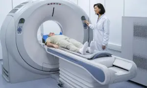 Pacjent leży na stole rezonansu magnetycznego, przygotowywany do badania. Lekarka w białym fartuchu obsługuje konsolę.