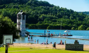 Słoneczny dzień na kąpielisku Stara Morawa. Ludzie odpoczywają na plaży, pływają i korzystają z uroków jeziora. W tle zielone wzgórza.