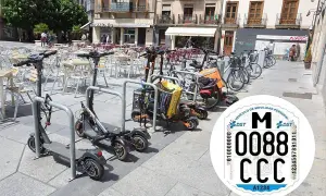 Patinetes eléctricos y bicicletas aparcados en una plaza. Se ve una pegatina de la DGT con la matricula CD.