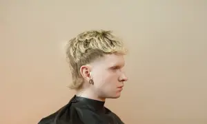 Młody mężczyzna z blond, kręconymi włosami i charakterystyczną fryzurą mullet.