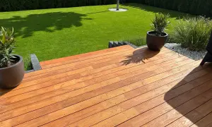 Terraza de madera de robinia con césped verde y plantas en macetas.