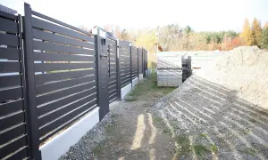 Schemat fundamentu pod bramę przesuwną. Widać nowoczesne ogrodzenie, materiały budowlane i hałdę żwiru.