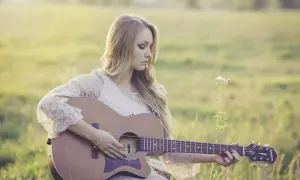 Dziewczyna gra na gitarze w plenerze. Czy wiesz, że gitara akustyczna ma swoje ciekawostki o muzyce?