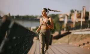 Donna con cuffie corre 10 km su un ponte, concentrata e determinata, con la treccia che ondeggia al vento.
