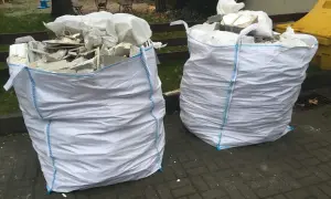 Dwa białe worki na gruz z niebieskimi szwami, gotowe do odbioru. W środku widać resztki materiałów budowlanych.