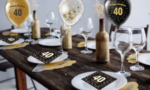 Elegancko udekorowany stół na 40 urodziny: złote i czarne balony, kieliszki, butelki i serwetki z cyfrą 40.