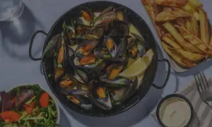 Un plat de moules frites, accompagné d'une salade fraîche et d'une sauce crémeuse. Un délice pour les amateurs de fruits de mer.