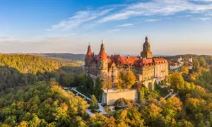Zamek Książ w malowniczej kotlinie kłodzkiej, otoczony jesiennymi barwami lasów, prezentuje się majestatycznie na tle błękitnego nieba.