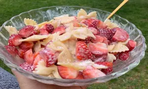 Makaron farfalle z kawałkami świeżych truskawek, polany kremowym sosem. Letnia uczta w misce.