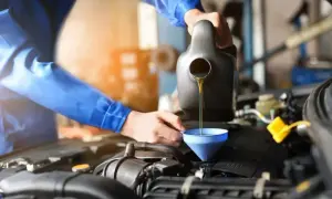 Mechanik w niebieskim kombinezonie nalewa olej silnikowy do silnika samochodu. To ważny element, by silnik działał jak nowy, a nie jak stara benzyna lakowa.