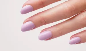 Une main aux ongles courts et arrondis, peints d'un joli violet pastel. Une idée ongle violet douce et élégante.