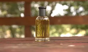 Szklana butelka perfum Boss Bottled Intense, z płynem o bursztynowym kolorze, stoi na drewnianym stole.