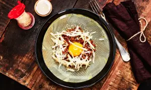 En läcker koreansk råbiff med en glänsande äggula i mitten, toppad med strimlad rättika och sesamfrön. Serveras på en vacker tallrik med en mörk servett och gaffel.