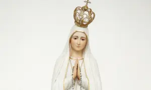 Figurka Matki Bożej Fatimskiej w białym welonie i złotej koronie, z rękami złożonymi do modlitwy.