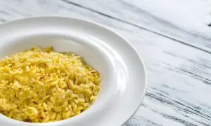 Un crémeux risotto à la milanaise, parsemé de fils de safran, dans une assiette blanche sur fond de bois.
