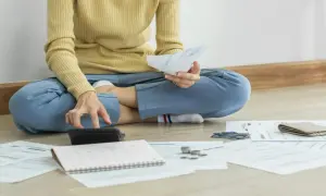 Osoba siedząca na podłodze z dokumentami, kalkulatorem i portfelem.