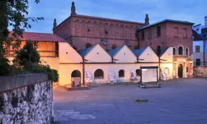 Stara synagoga w Krakowie o zmierzchu. Ceglana fasada, jasne przybudówki i kamienny dziedziniec tworzą historyczny klimat.